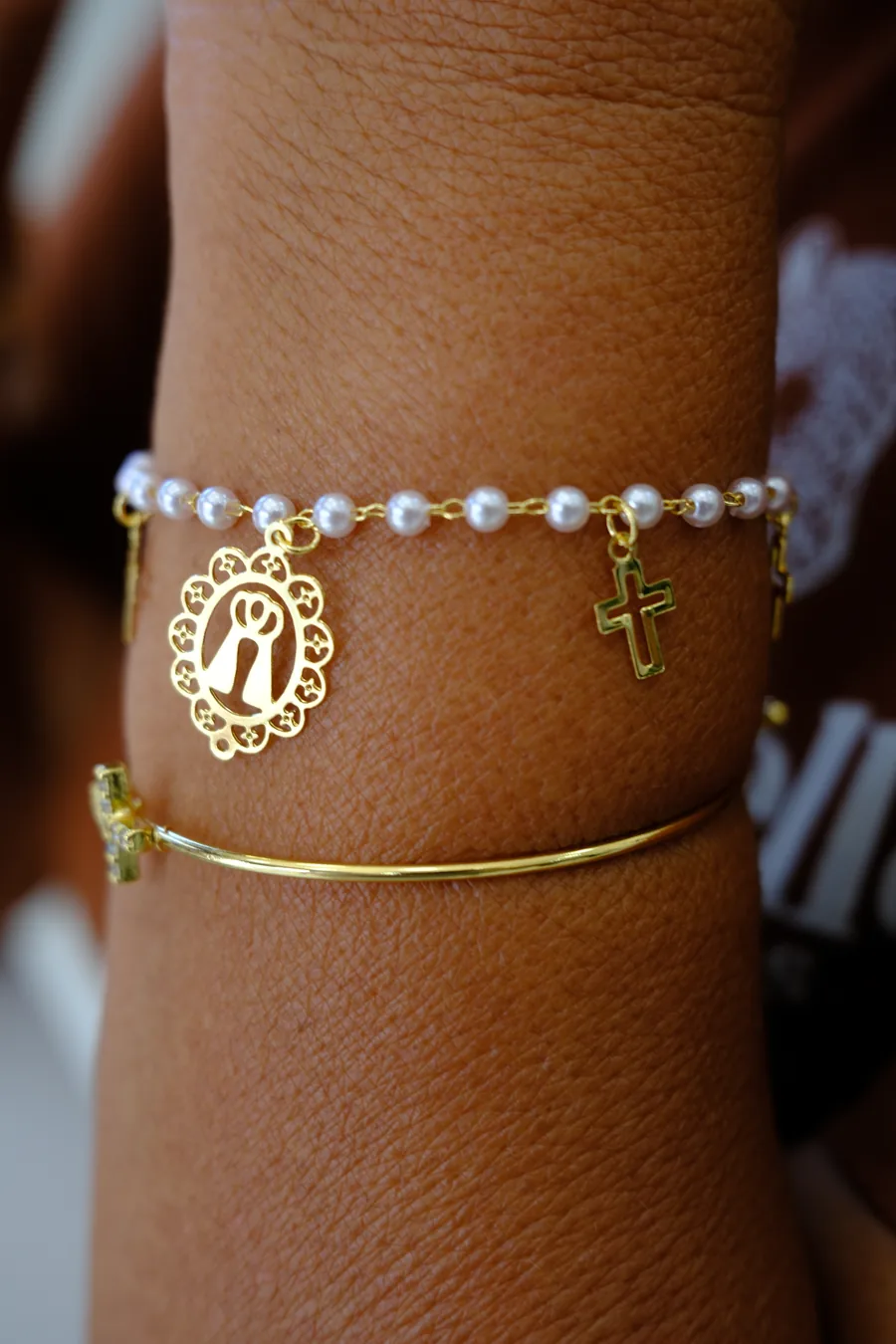 Pulseiras douradas com pérolas e medalha no pulso